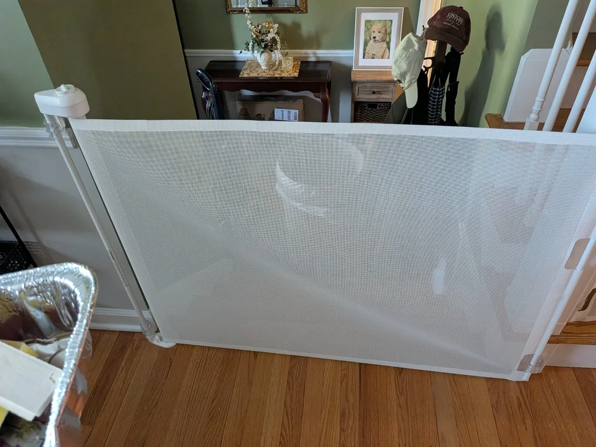 A retractable mesh safety gate installed across a hallway opening beside a staircase.