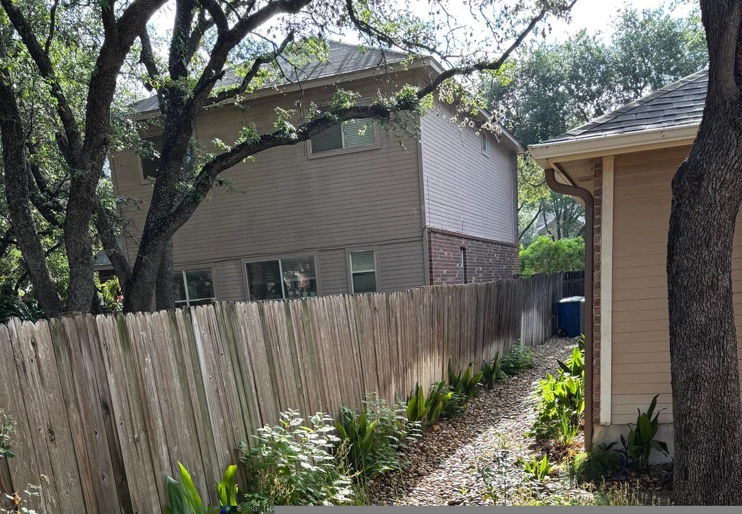 Finished rain garden with a river-rock channel and native plants beside a house.